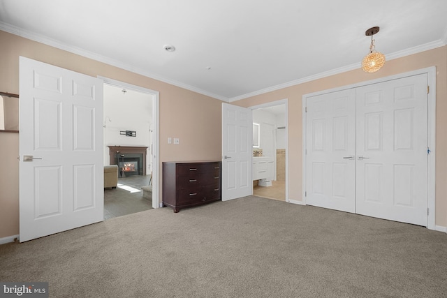 unfurnished bedroom featuring a glass covered fireplace, a closet, carpet flooring, crown molding, and baseboards