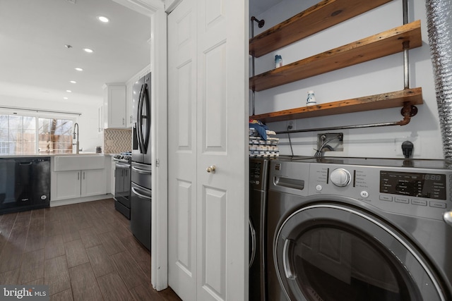 clothes washing area with dark wood-type flooring, washer and clothes dryer, laundry area, recessed lighting, and a sink