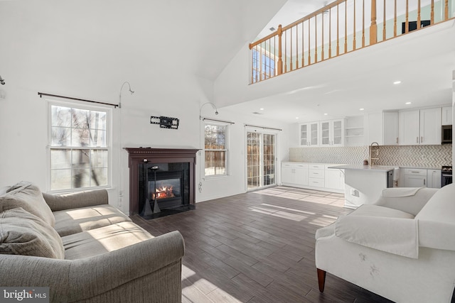 living area featuring a high ceiling, a fireplace with flush hearth, light wood-style floors, and recessed lighting