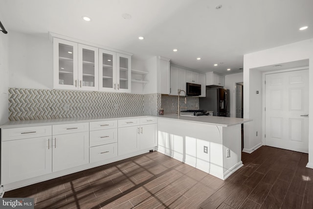 kitchen with wood finish floors, refrigerator with ice dispenser, stainless steel microwave, a peninsula, and light countertops