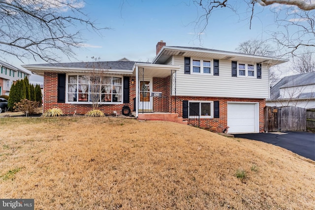 tri-level home with a front yard, driveway, a chimney, a garage, and brick siding