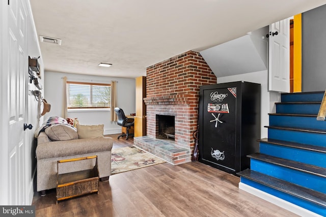 living area with stairs, a brick fireplace, wood finished floors, and visible vents