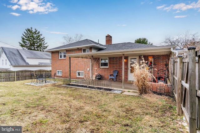 rear view of property with fence, a chimney, a lawn, a patio area, and brick siding