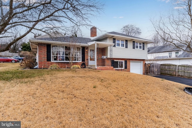 tri-level home with a front yard, fence, brick siding, and a chimney