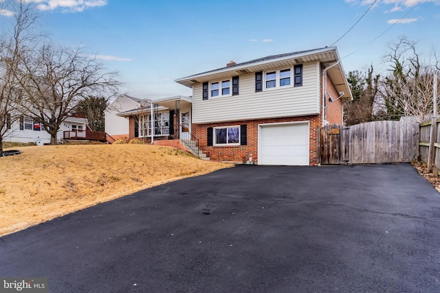 tri-level home featuring aphalt driveway, brick siding, a garage, and fence