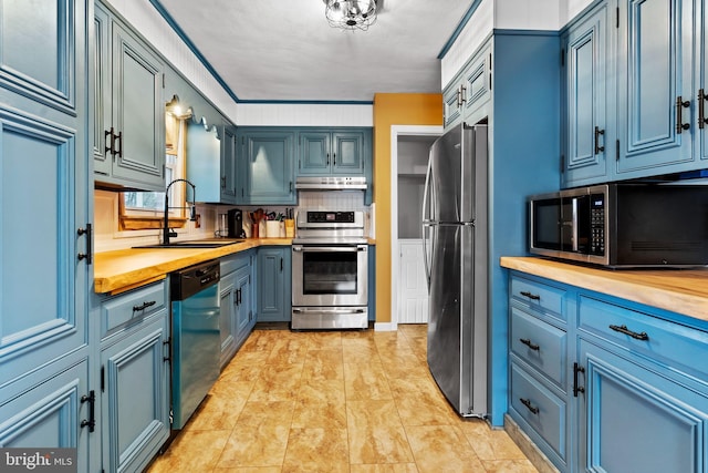 kitchen featuring under cabinet range hood, blue cabinetry, a sink, appliances with stainless steel finishes, and butcher block counters