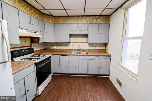 kitchen featuring gray cabinetry, under cabinet range hood, a drop ceiling, gas range, and a sink