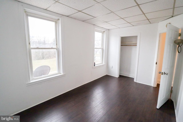 unfurnished bedroom with a drop ceiling, a closet, and dark wood-style floors