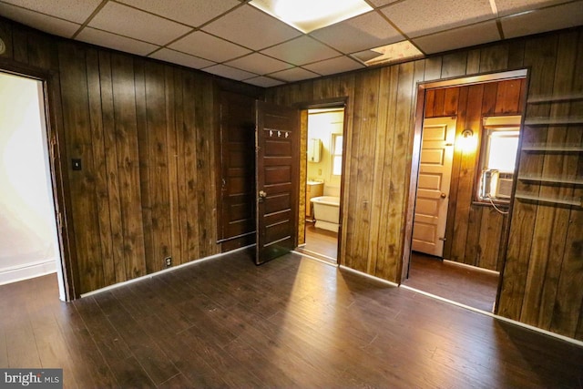 unfurnished bedroom featuring wooden walls, cooling unit, wood finished floors, a paneled ceiling, and ensuite bathroom