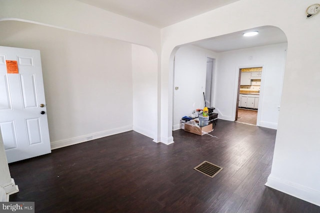 spare room with wood finished floors, visible vents, arched walkways, and baseboards