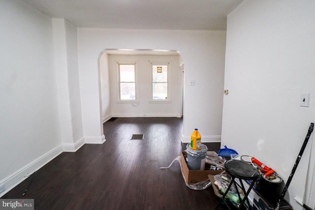 interior space featuring wood finished floors, visible vents, arched walkways, and baseboards