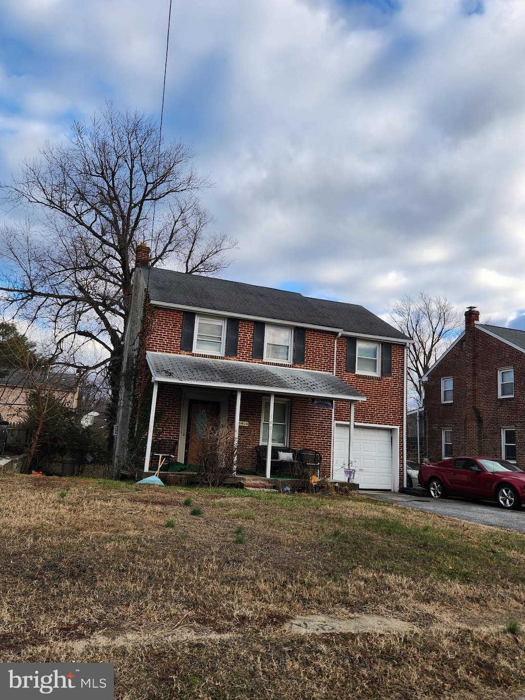 traditional home featuring a porch, a garage, brick siding, driveway, and a chimney