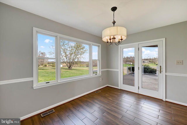 unfurnished dining area featuring baseboards, dark wood-type flooring, visible vents, and a chandelier