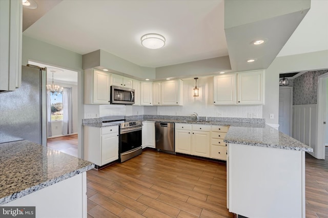 kitchen featuring a sink, appliances with stainless steel finishes, white cabinetry, a peninsula, and a notable chandelier