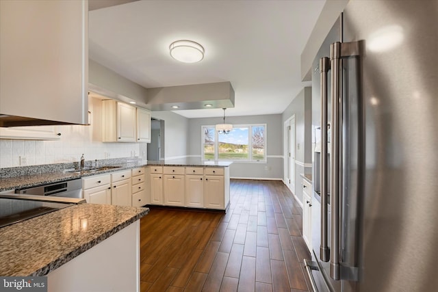 kitchen featuring dark stone countertops, high end fridge, baseboards, a peninsula, and dark wood-style flooring