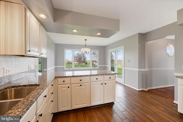kitchen with a peninsula, tasteful backsplash, baseboards, light stone counters, and dark wood-type flooring
