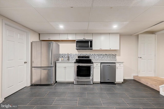 kitchen with white cabinets, a paneled ceiling, appliances with stainless steel finishes, and light stone counters