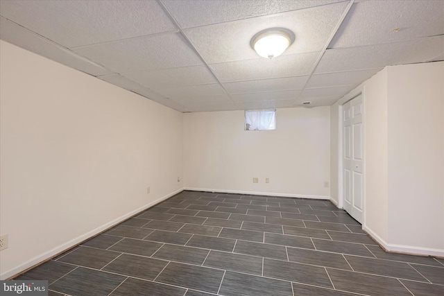 basement featuring a paneled ceiling and baseboards