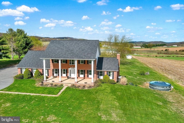 rear view of house with a lawn, a chimney, dirt driveway, a patio, and brick siding