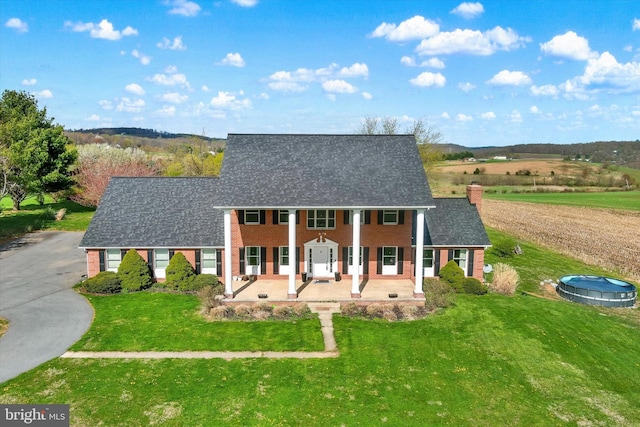 view of front of home with a front lawn, driveway, a chimney, covered porch, and brick siding