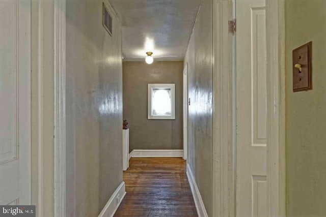 hall with dark wood-type flooring, visible vents, and baseboards