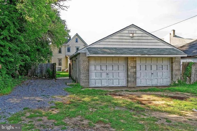 view of front of property with an outbuilding, a shingled roof, a detached garage, and fence