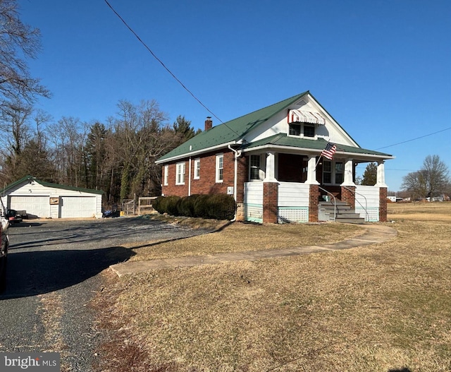 bungalow featuring brick siding, a porch, a chimney, a garage, and an outbuilding