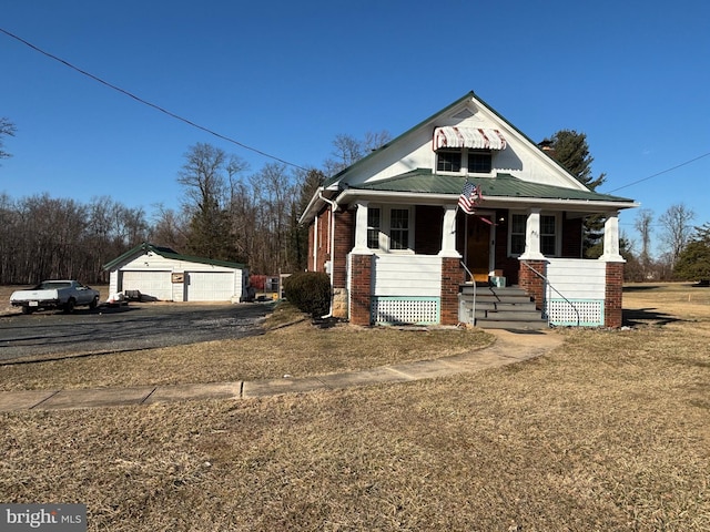 bungalow-style house featuring brick siding, covered porch, metal roof, a garage, and an outdoor structure