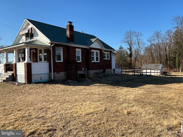 view of property exterior with brick siding, fence, a chimney, metal roof, and a yard