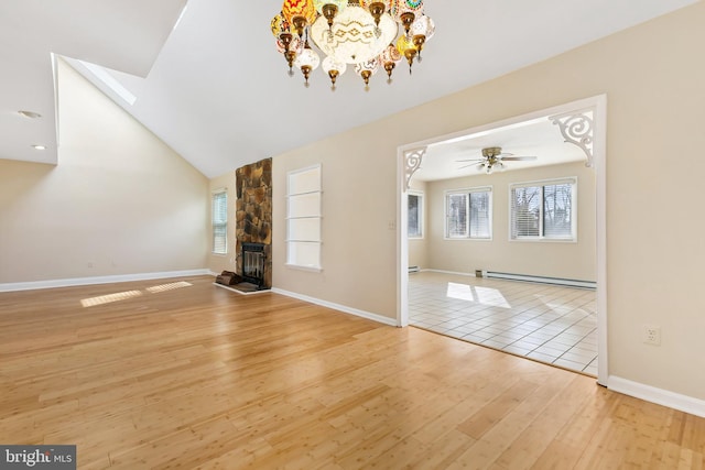 unfurnished living room featuring baseboards, light wood-style flooring, a stone fireplace, a baseboard heating unit, and ceiling fan with notable chandelier