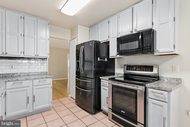 kitchen with light tile patterned floors, black appliances, light countertops, white cabinetry, and backsplash