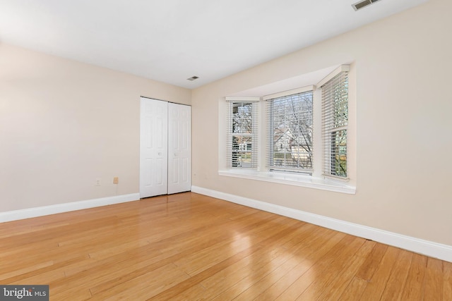 unfurnished bedroom with a closet, visible vents, light wood-type flooring, and baseboards