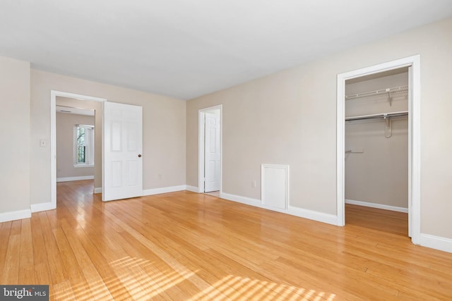 unfurnished bedroom with a closet, light wood-style flooring, a walk in closet, and baseboards