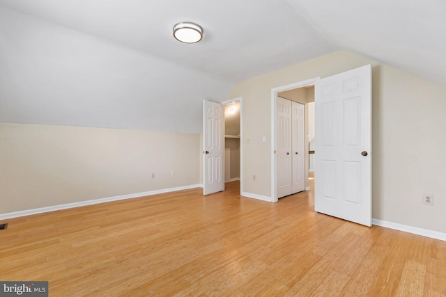 additional living space with baseboards, light wood-style floors, and vaulted ceiling