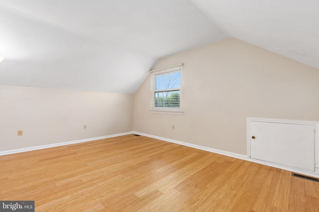 additional living space with light wood-type flooring, baseboards, visible vents, and vaulted ceiling