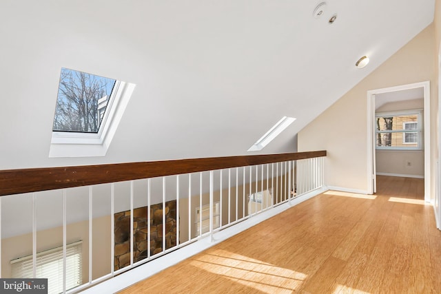 corridor featuring baseboards, vaulted ceiling with skylight, and wood finished floors