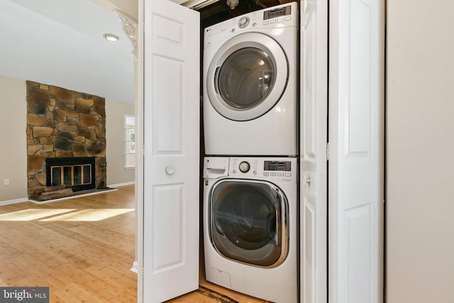 washroom with baseboards, laundry area, light wood-style flooring, a fireplace, and stacked washer / drying machine