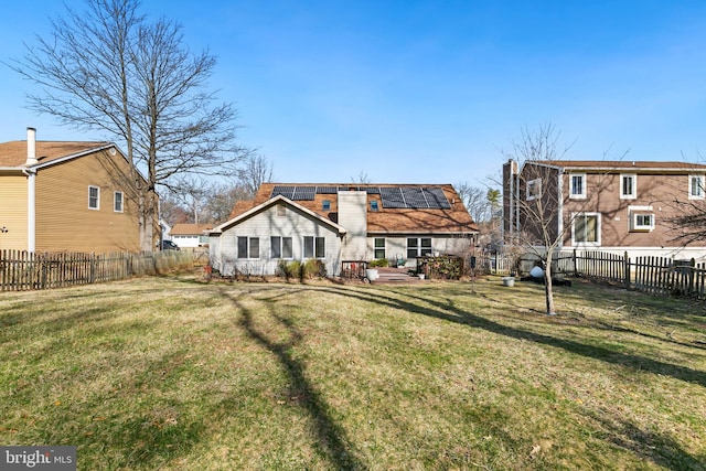 rear view of house featuring a yard, roof mounted solar panels, a chimney, and a fenced backyard