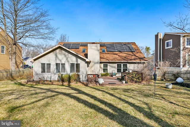 rear view of house featuring solar panels, a lawn, fence, and a chimney