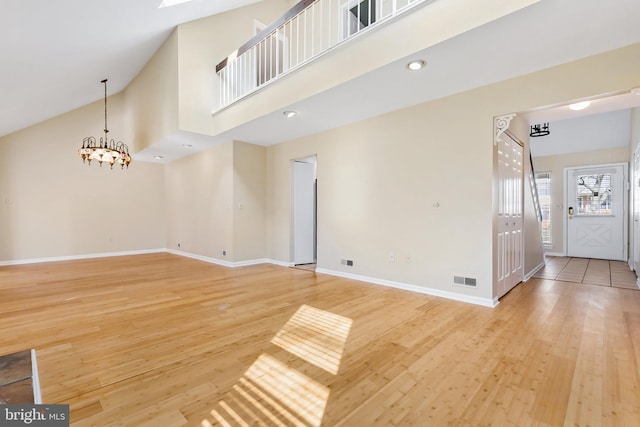 unfurnished living room featuring visible vents, high vaulted ceiling, a notable chandelier, light wood-style floors, and baseboards