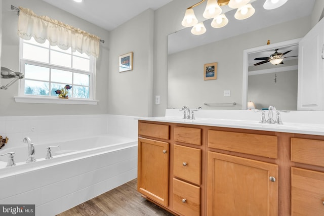 bathroom with a garden tub, double vanity, wood finished floors, a ceiling fan, and a sink