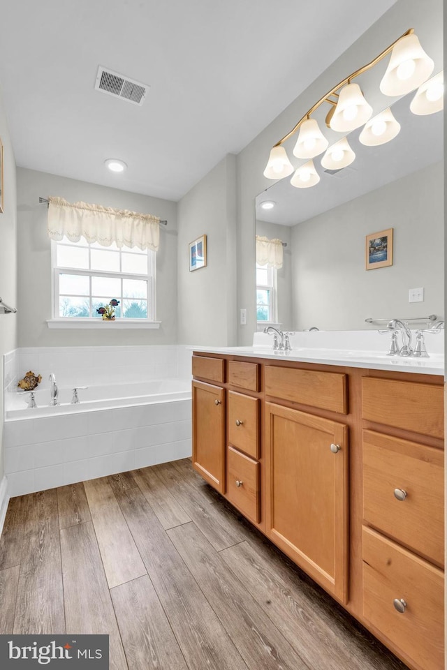 bathroom with wood finished floors, visible vents, double vanity, a sink, and a garden tub