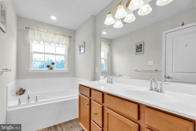 full bath with a bath, double vanity, wood finished floors, and a sink