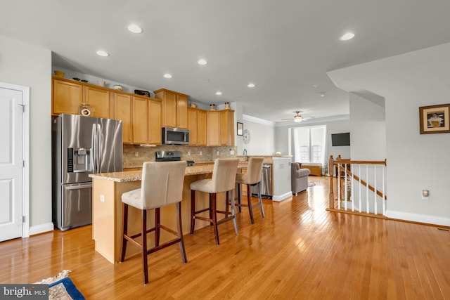 kitchen with a kitchen bar, light wood-style flooring, stainless steel appliances, decorative backsplash, and light stone countertops