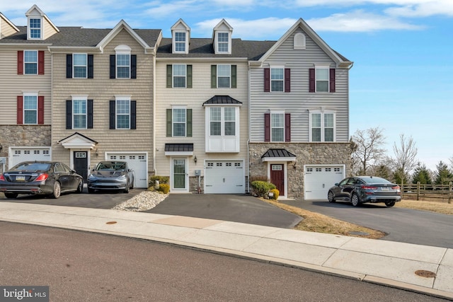 view of property featuring an attached garage, stone siding, and driveway