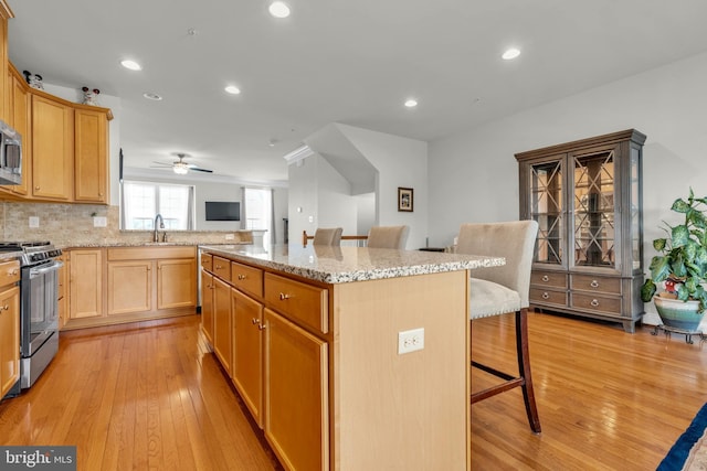 kitchen featuring a breakfast bar area, light stone counters, recessed lighting, a sink, and appliances with stainless steel finishes