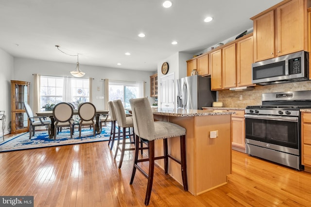 kitchen with tasteful backsplash, light stone countertops, a breakfast bar, light wood-style flooring, and appliances with stainless steel finishes