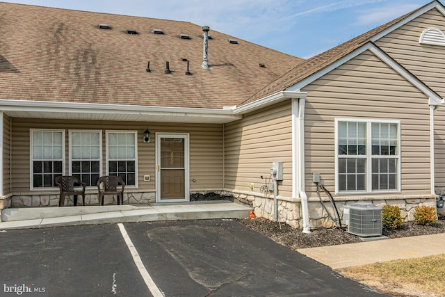 exterior space with stone siding, central AC, and a shingled roof