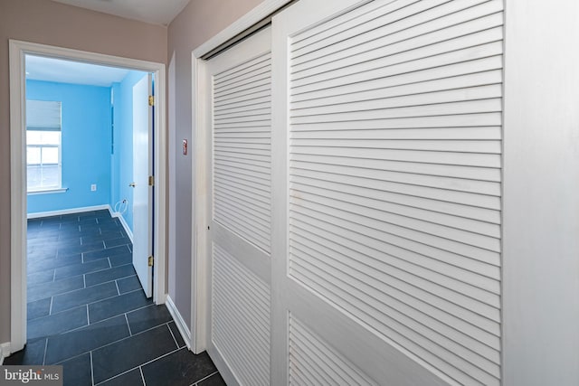 corridor with dark tile patterned floors and baseboards