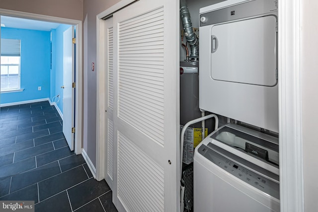 washroom featuring baseboards, stacked washer and dryer, laundry area, and dark tile patterned flooring